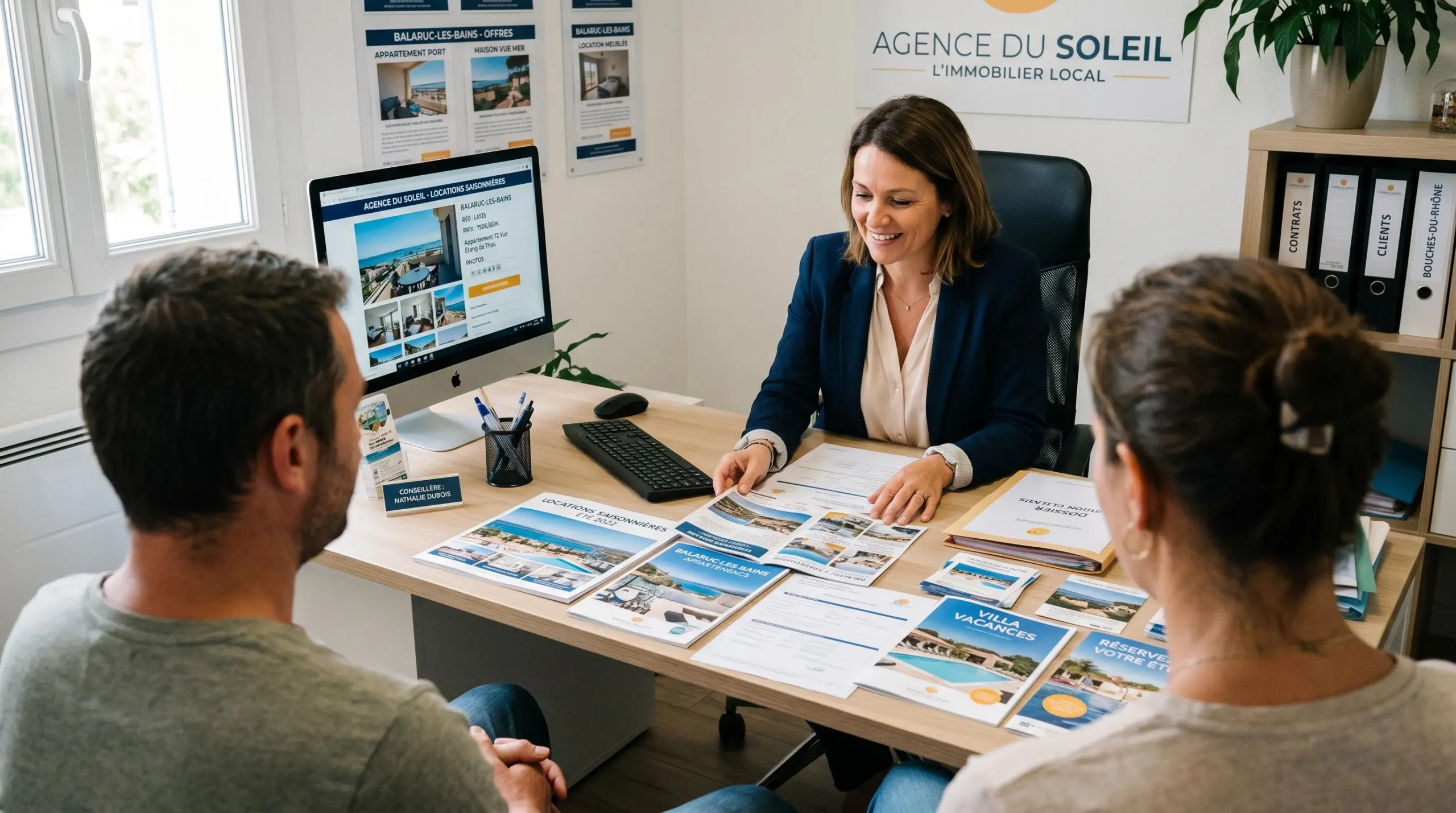 Conseillère immobilière dans une agence à Balaruc-les-Bains présentant des documents de location saisonnière à un couple de clients, bureau contemporain avec écran et brochures