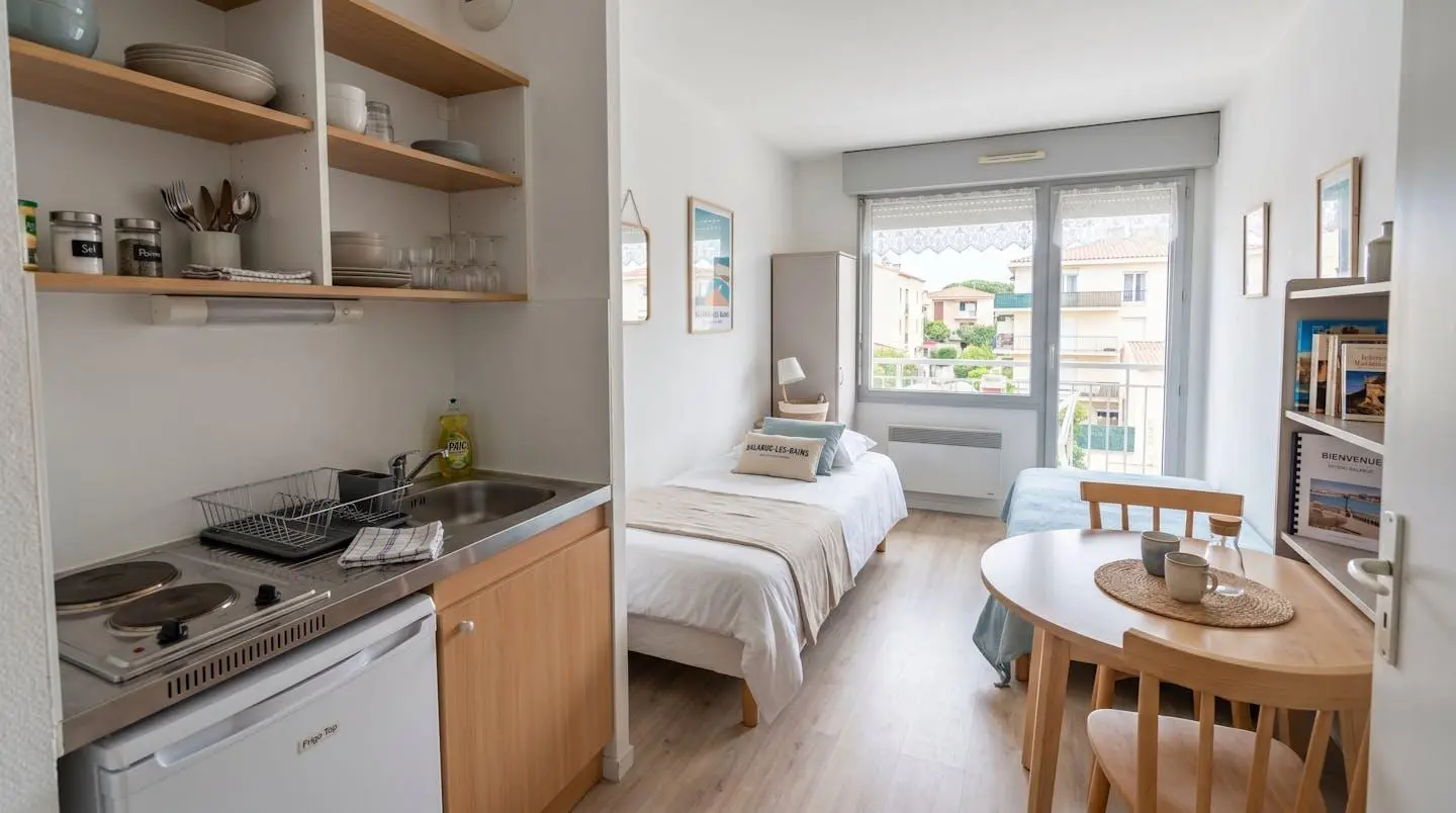 Intérieur d'un studio meublé de tourisme de 20 m² à Balaruc-les-Bains avec coin cuisine équipé, lit et table, décoration épurée tons clairs et lumière naturelle
