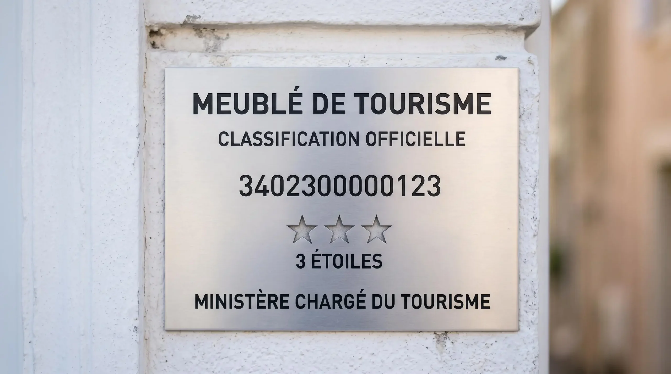 Gros plan sur une plaque officielle de numéro d'enregistrement d'un meublé de tourisme classé avec étoiles, apposée sur le mur extérieur d'un immeuble à Balaruc-les-Bains