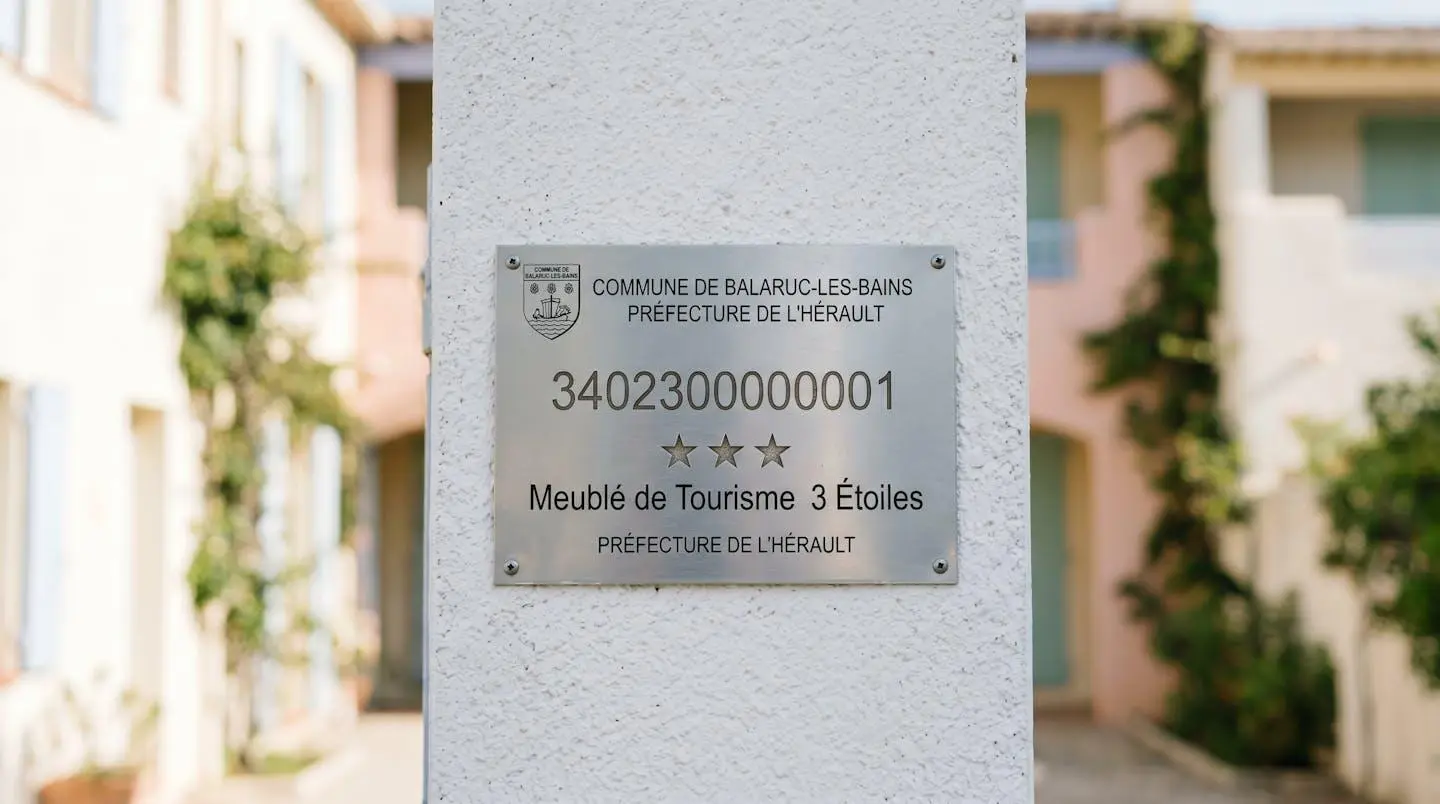 Gros plan sur une plaque officielle de numéro d'enregistrement d'un meublé de tourisme classé avec étoiles, apposée sur le mur extérieur d'un immeuble à Balaruc-les-Bains