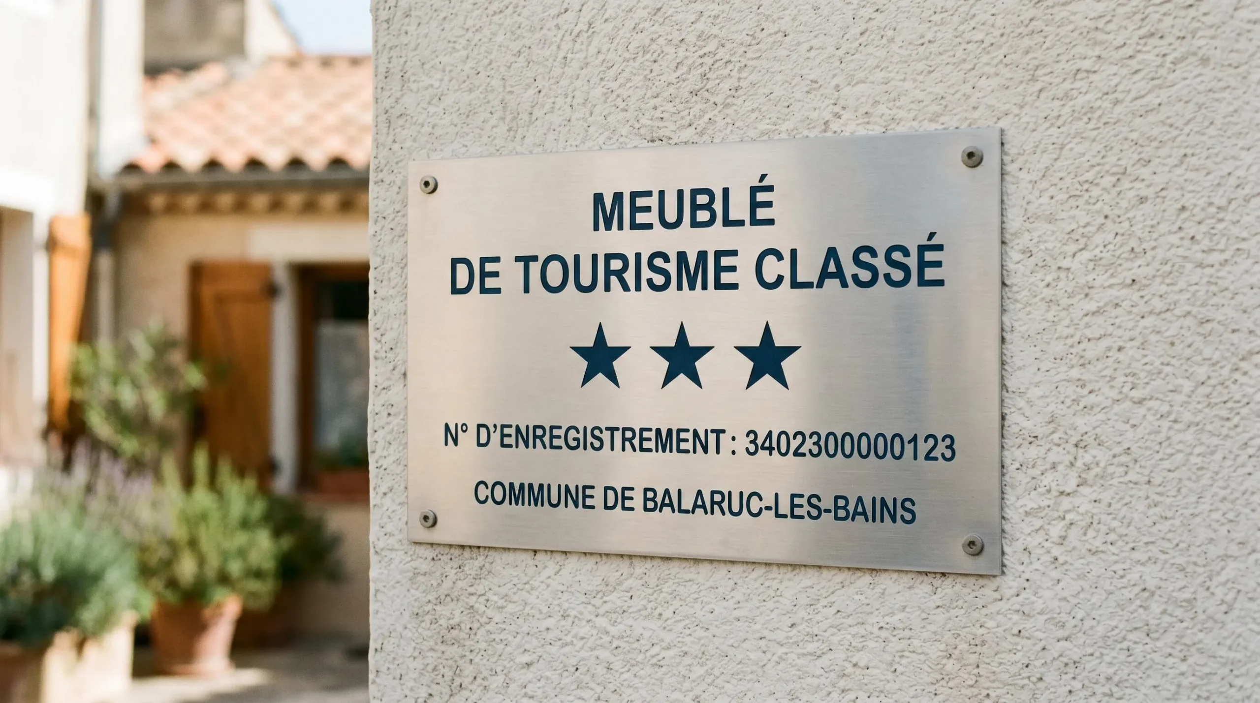 Gros plan sur une plaque officielle de numéro d'enregistrement d'un meublé de tourisme classé avec étoiles, apposée sur le mur extérieur d'un immeuble à Balaruc-les-Bains
