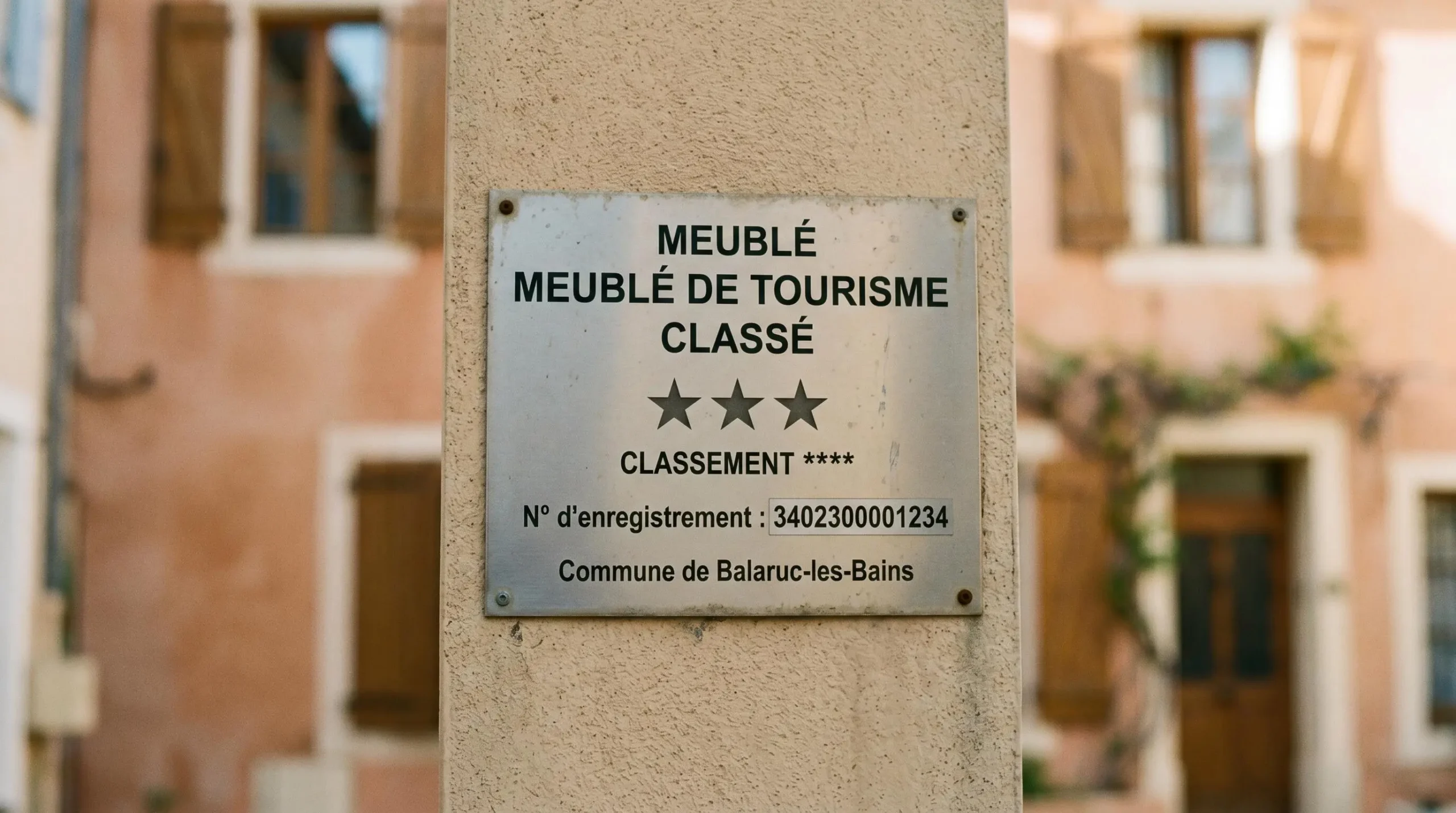 Gros plan sur une plaque officielle de numéro d'enregistrement d'un meublé de tourisme classé avec étoiles, apposée sur le mur extérieur d'un immeuble à Balaruc-les-Bains