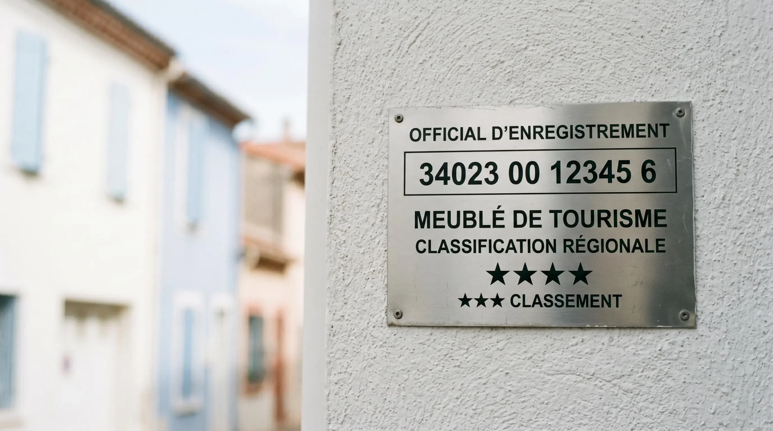 Gros plan sur une plaque officielle de numéro d'enregistrement d'un meublé de tourisme classé avec étoiles, apposée sur le mur extérieur d'un immeuble à Balaruc-les-Bains
