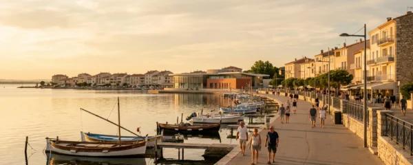 Vue panoramique de la promenade du bord de l'étang de Thau à Balaruc-les-Bains en lumière dorée de fin d'après-midi, avec l'établissement thermal en arrière-plan et des bateaux de pêche traditionnels amarrés